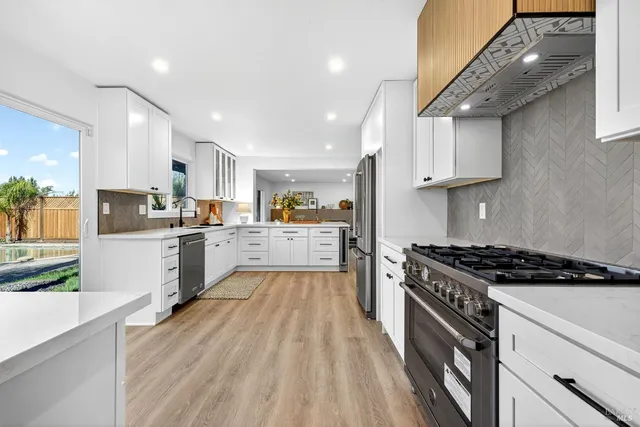 a large kitchen with kitchen island a sink dishwasher stove and white cabinets next to a window