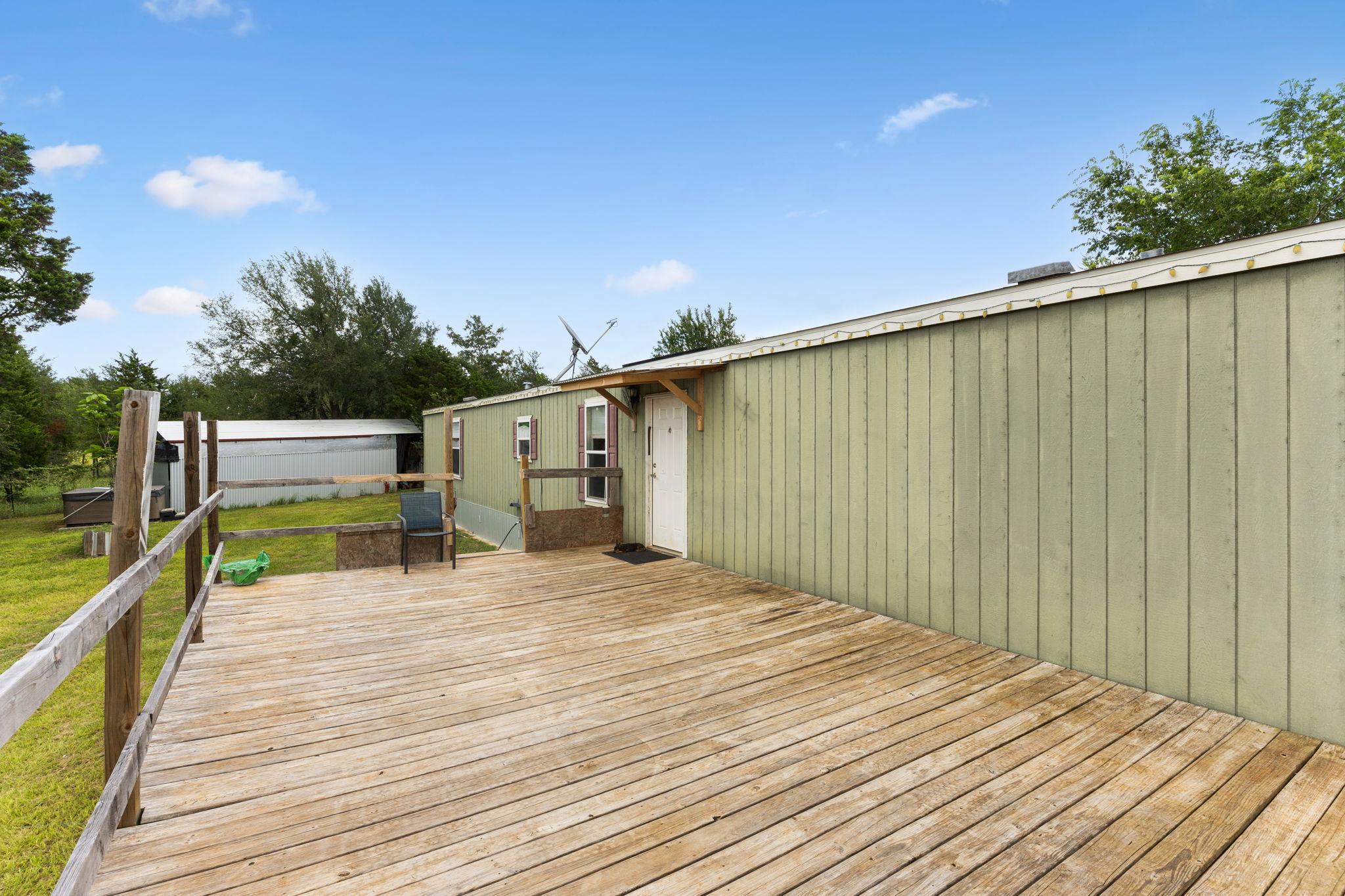 253 North County Line Road, Unit C Elgin, TX 78621 - Photo 4 of 39 A spacious wooden deck extends from a verdant green dwelling, perfect for outdoor enjoyment.