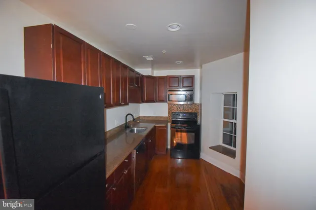 a kitchen with granite countertop a refrigerator a sink and wooden cabinets
