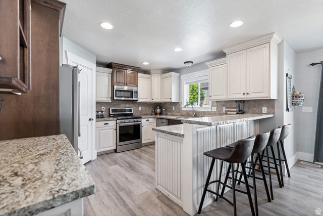 580 Cherry Ridge Lane Richmond, UT 84333 - Photo 12 of 53 Kitchen with stainless steel appliances, a peninsula, light wood-style floors, a breakfast bar area, and light stone countertops