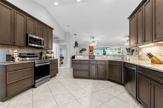 a kitchen with stainless steel appliances granite countertop a stove top oven a sink dishwasher and a refrigerator with wooden cabinets