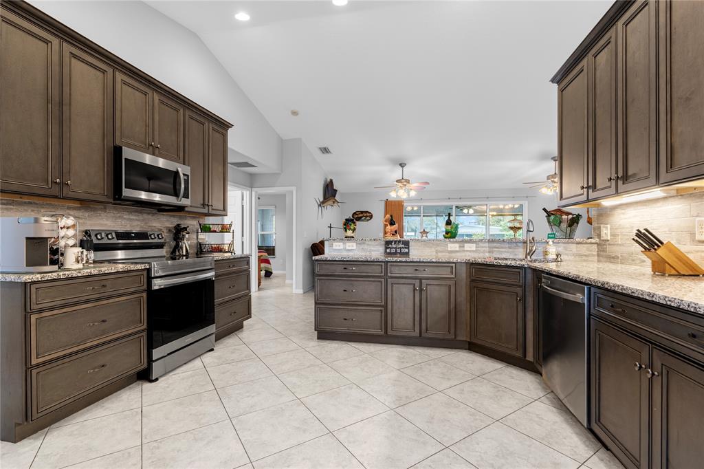 1069 9th Street Okeechobee, FL 34974 - Photo 19 of 48 a kitchen with stainless steel appliances granite countertop a stove top oven a sink dishwasher and a refrigerator with wooden cabinets
