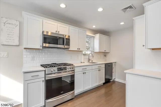 a kitchen with stainless steel appliances granite countertop white cabinets a sink a stove a microwave and cabinetry