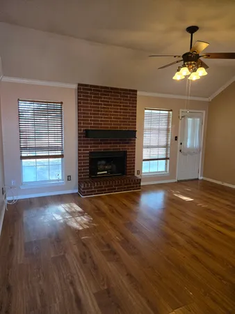 a view of an empty room with wooden floor fireplace and a window