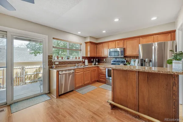 a kitchen with stainless steel appliances granite countertop wooden cabinets a sink a stove a refrigerator with grey cabinets and wooden floor