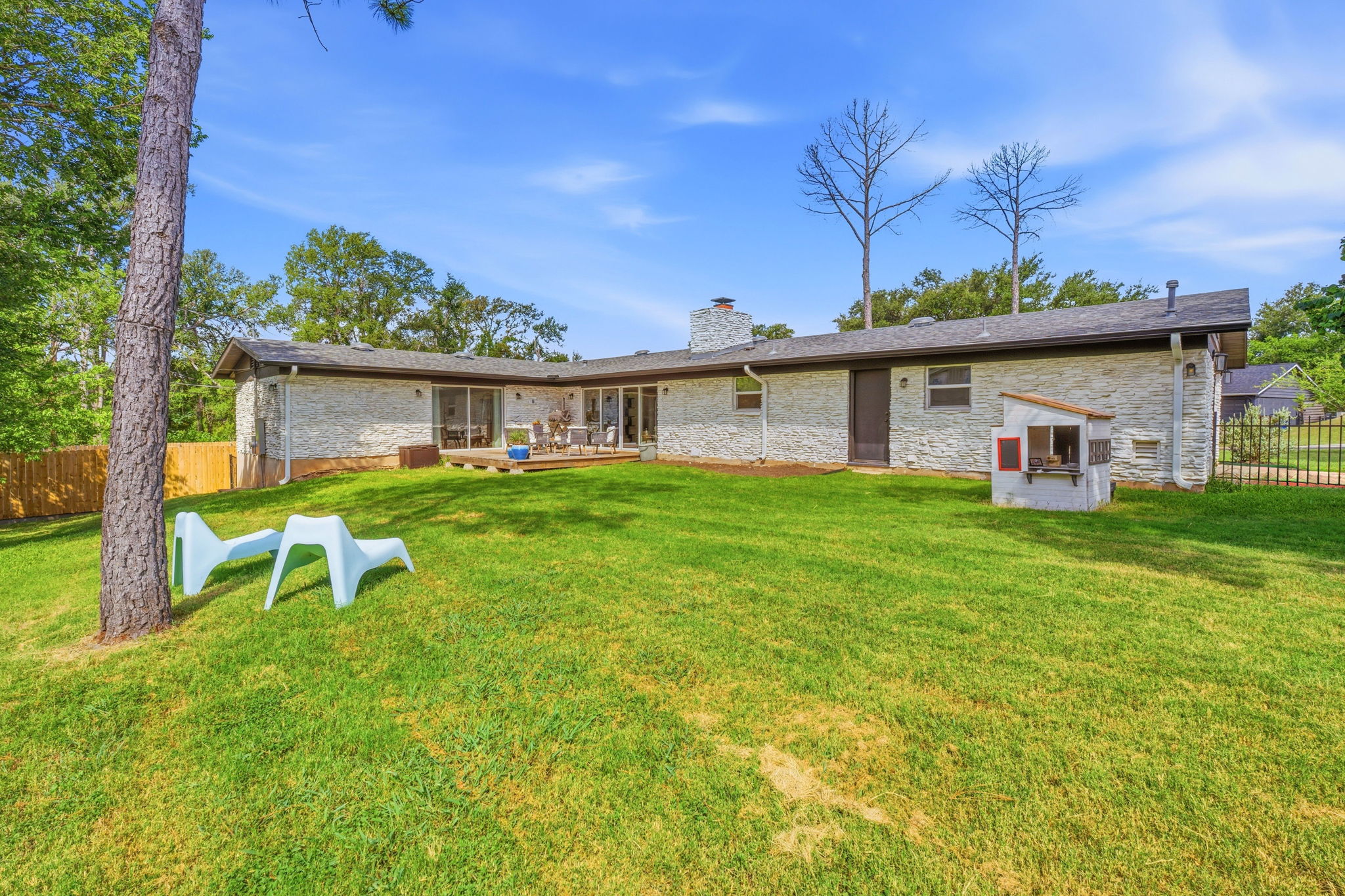 4403 Elmsgrove Drive Austin, TX 78721 - Photo 38 of 38 A verdant backyard with a wooden deck invites outdoor leisure, bordered by a privacy fence and natural landscaping.