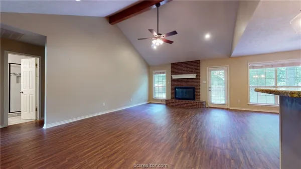 a view of an empty room with wooden floor fireplace and a window