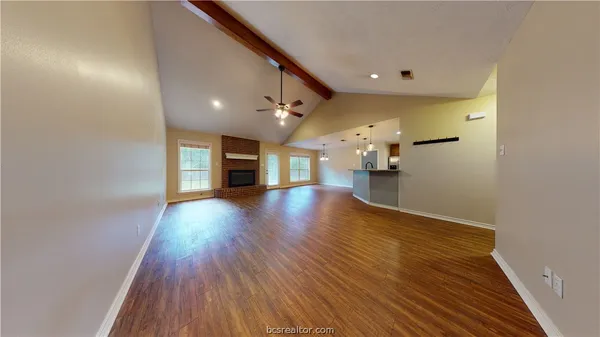 a view of an empty room and a kitchen with wooden floor
