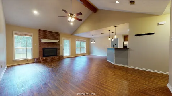 an empty room with wooden floor a ceiling fan a fireplace and windows