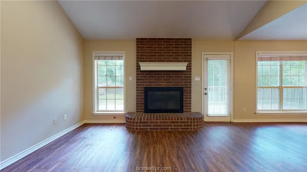 an empty room with wooden floor a fireplace and windows