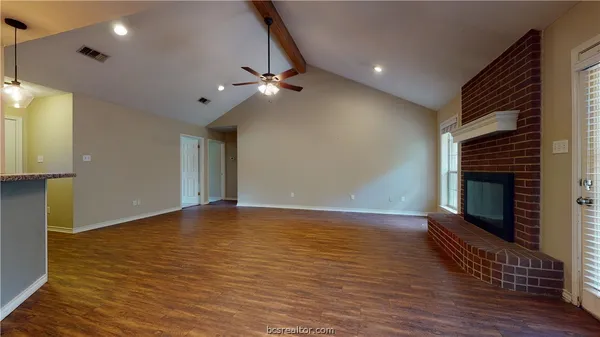 a view of an empty room with wooden floor and a fireplace