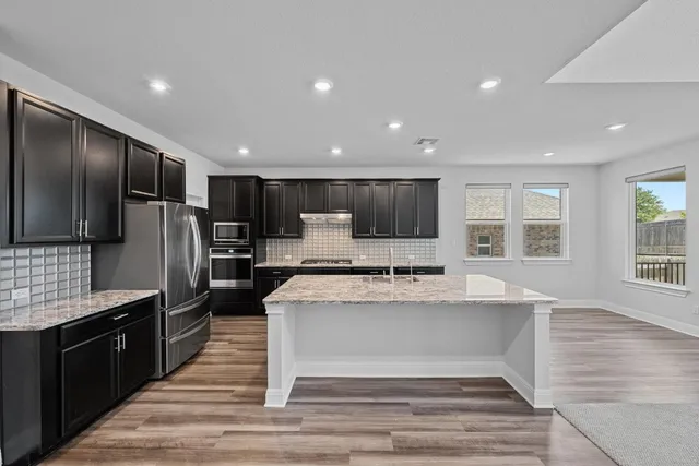 a large kitchen with kitchen island a large counter top stainless steel appliances and cabinets