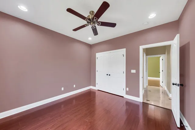 a view of an empty room with wooden floor and a ceiling fan