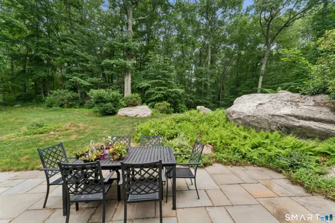 a view of a backyard with table and chairs potted plants and large tree