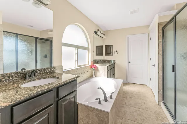 a en suite bathroom with a granite countertop double vanity sink a mirror and a bathtub