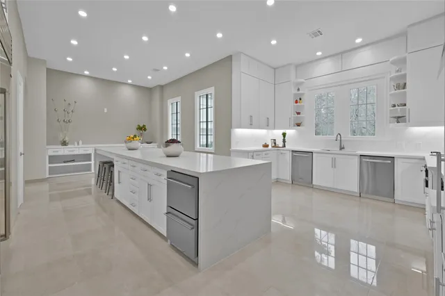 a large white kitchen with center island and stainless steel appliances