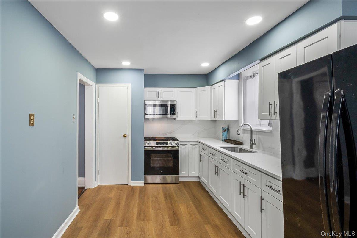 196-19 89th Road Queens, NY 11423 - Photo 8 of 28 a large kitchen with a stove a sink dishwasher a refrigerator and white cabinets with wooden floor