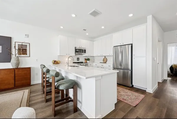a kitchen with stainless steel appliances kitchen island granite countertop a refrigerator a stove a sink a dining table and chairs with wooden floor