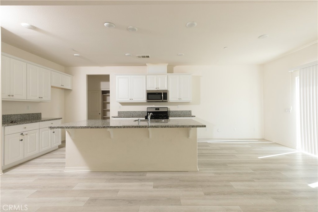 4875 Prairie Run Road Eastvale, CA 91752 - Photo 4 of 18 a large kitchen with granite countertop a stove top oven a sink dishwasher and white cabinets with wooden floor