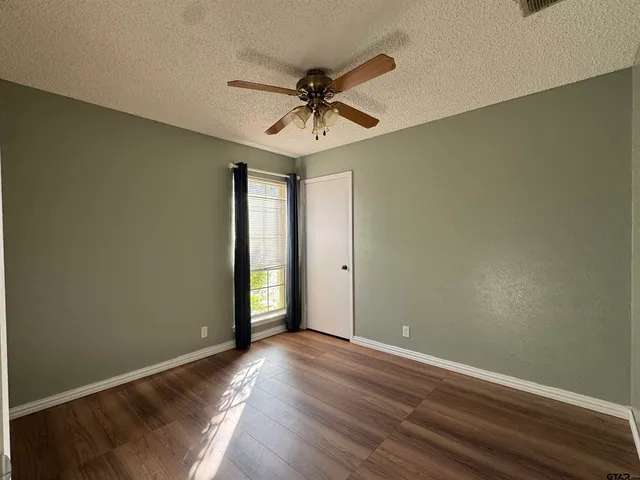 an empty room with wooden floor fan and windows