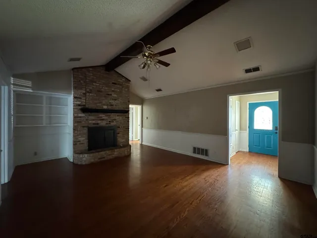 an empty room with wooden floor fireplace and windows