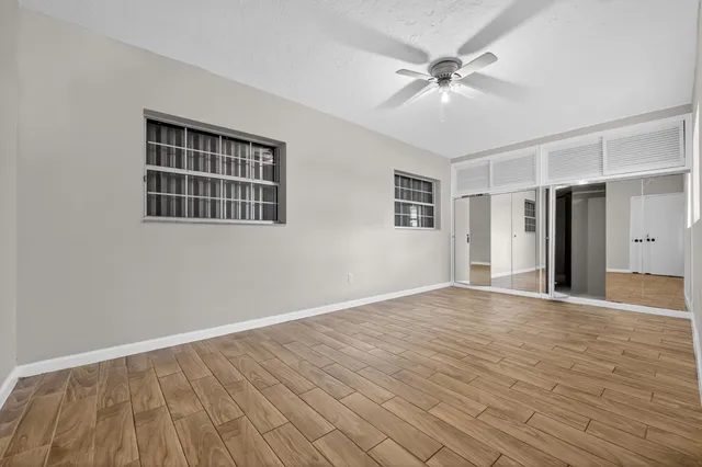 a view of an empty room with wooden floor and a ceiling fan