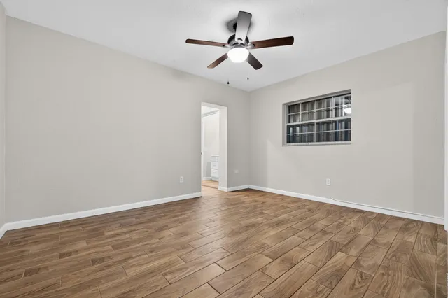 a view of an empty room with wooden floor and a ceiling fan