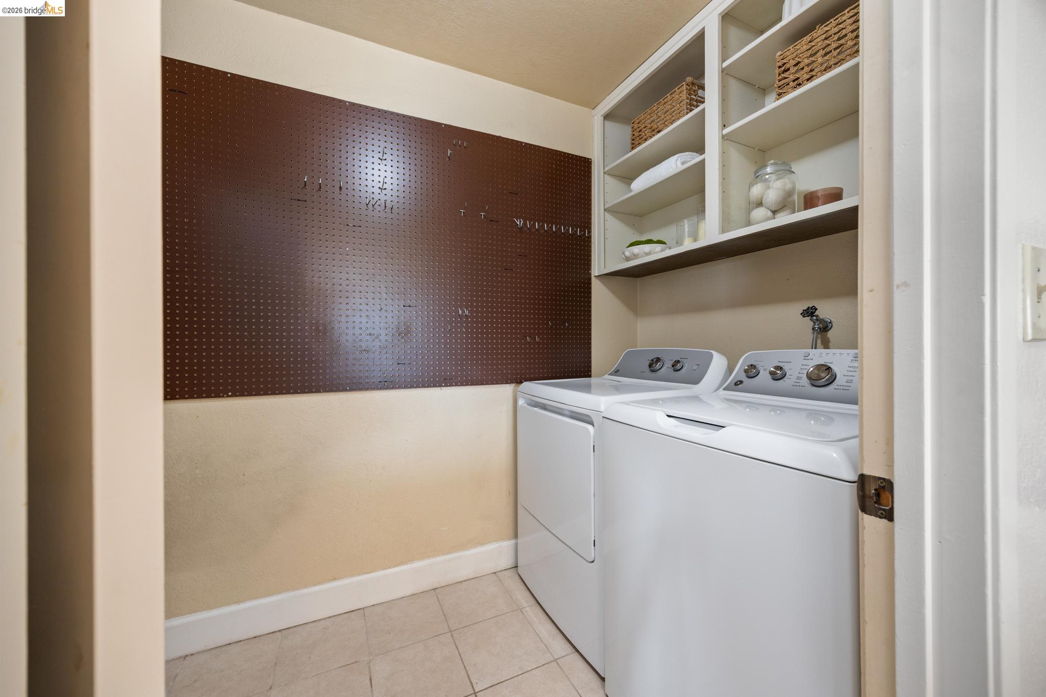 201 Vista Heights Road El Cerrito, CA 94530 - Photo 24 of 32 Dedicated laundry area featuring a brown pegboard wall, built-in open shelving, and neutral floor tiling