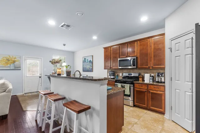 a kitchen with stainless steel appliances granite countertop a stove top oven a sink dishwasher a dining table and chairs with wooden floor