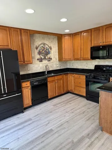 a kitchen with stainless steel appliances granite countertop wooden cabinets a refrigerator a stove a sink and dishwasher with wooden floor