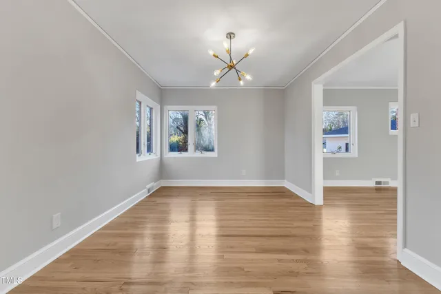 an empty room with wooden floor chandelier fan and windows