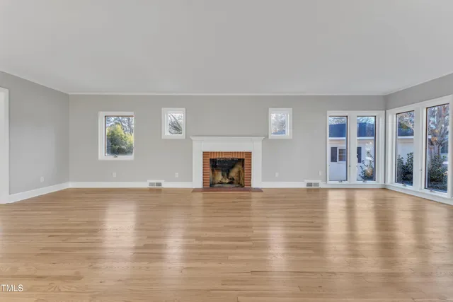 a view of an empty room with wooden floor and a fireplace
