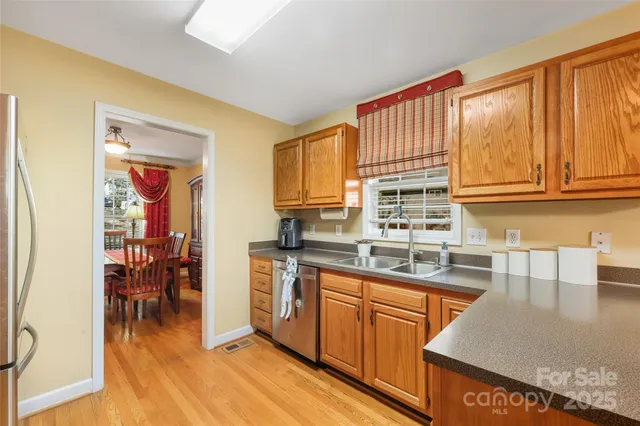 a kitchen with stainless steel appliances granite countertop a refrigerator a sink dishwasher a stove and a dining table with wooden floor