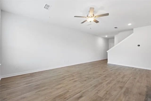 an empty room with wooden floor ceiling fan and windows