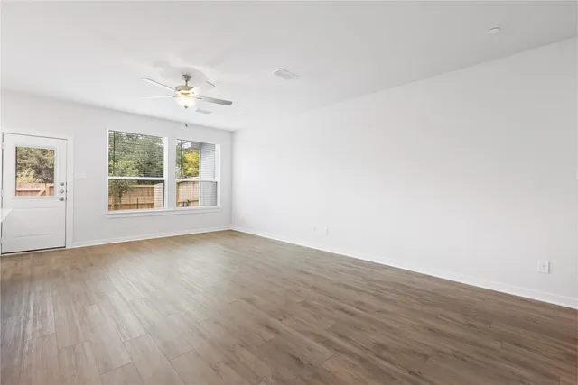 an empty room with wooden floor chandelier fan and windows