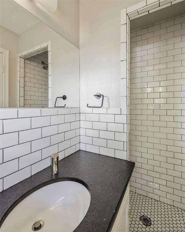 2323 Sutter Street Dallas, TX 75216 - Photo 19 of 30 Master Bathroom featuring a tile shower, tile walls, and large vanity