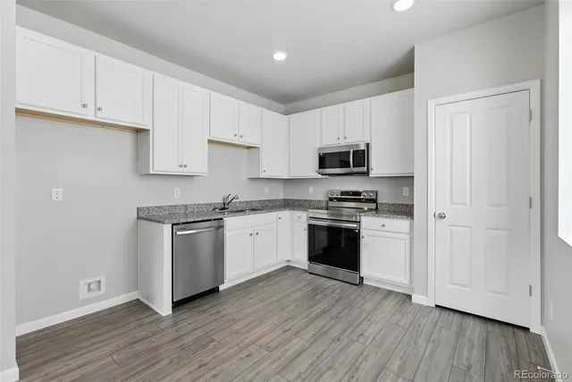 a kitchen with granite countertop white cabinets and stainless steel appliances with wooden floors