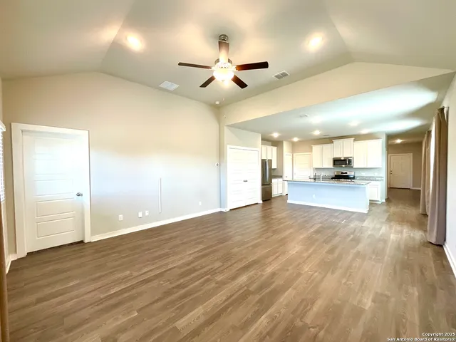 an empty room with wooden floor and a kitchen