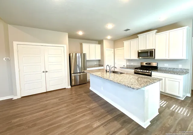 a large kitchen with granite countertop a stove a sink a refrigerator and white cabinets with wooden floor