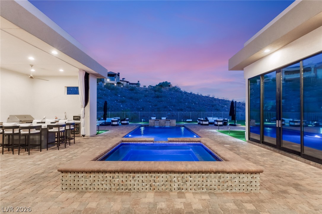 5 Crystal Tree Pass Henderson, NV 89052 - Photo 58 of 67 An inviting outdoor kitchen and two sparkling pools set against a stunning twilight mountain backdrop.