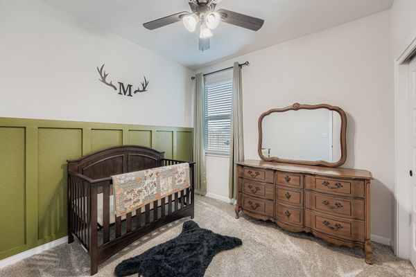 148 Gullivers Drive Elgin, TX 78621 - Photo 16 of 21 Bedroom featuring a decorative wall, a crib, ceiling fan, light carpet, and a wainscoted wall
