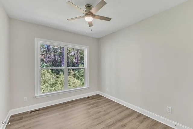 an empty room with wooden floor fan and windows
