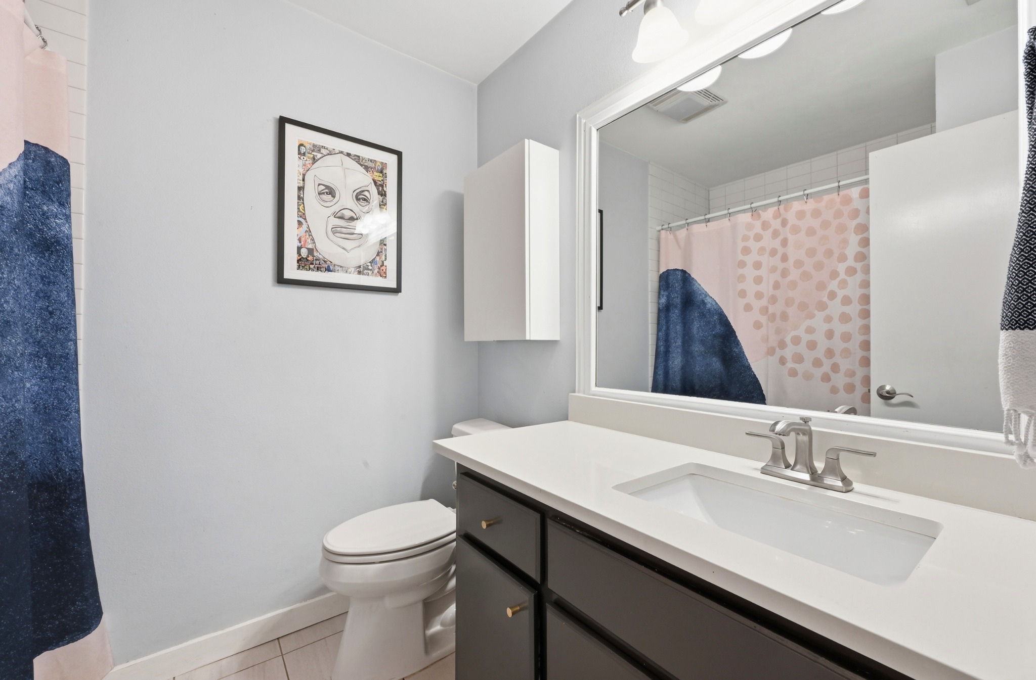 2509 Redleaf Lane Austin, TX 78745 - Photo 16 of 28 Bathroom featuring a vanity with a white countertop and dark cabinetry, an undermount sink with a brushed nickel faucet, a wall-mounted mirror, and tile flooring