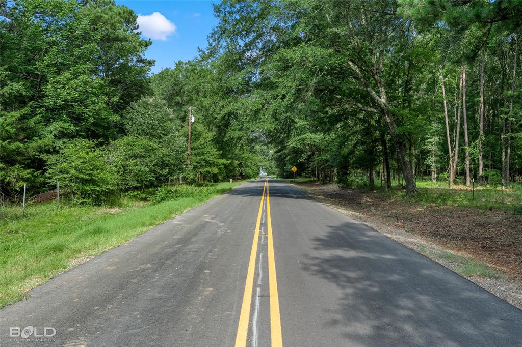 11015 Hereford Road Mooringsport, LA 71060 - Photo 9 of 18 Paved road with double yellow lines, bordered by mature trees and natural landscaping