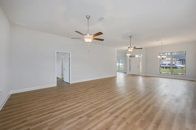 an empty room with wooden floor chandelier fan and windows