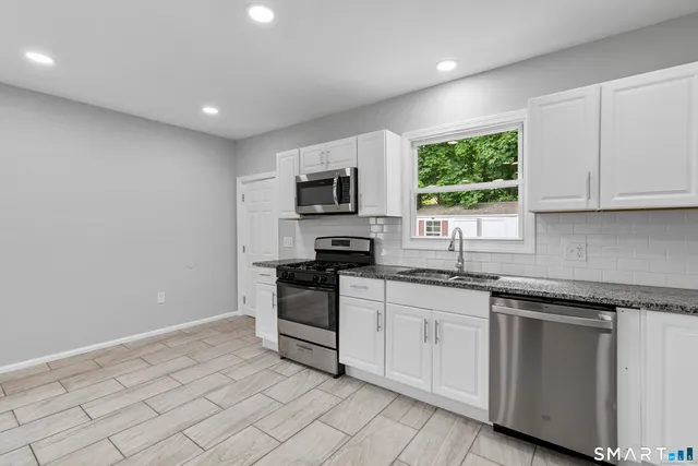 a kitchen with granite countertop white cabinets white appliances a sink and a window