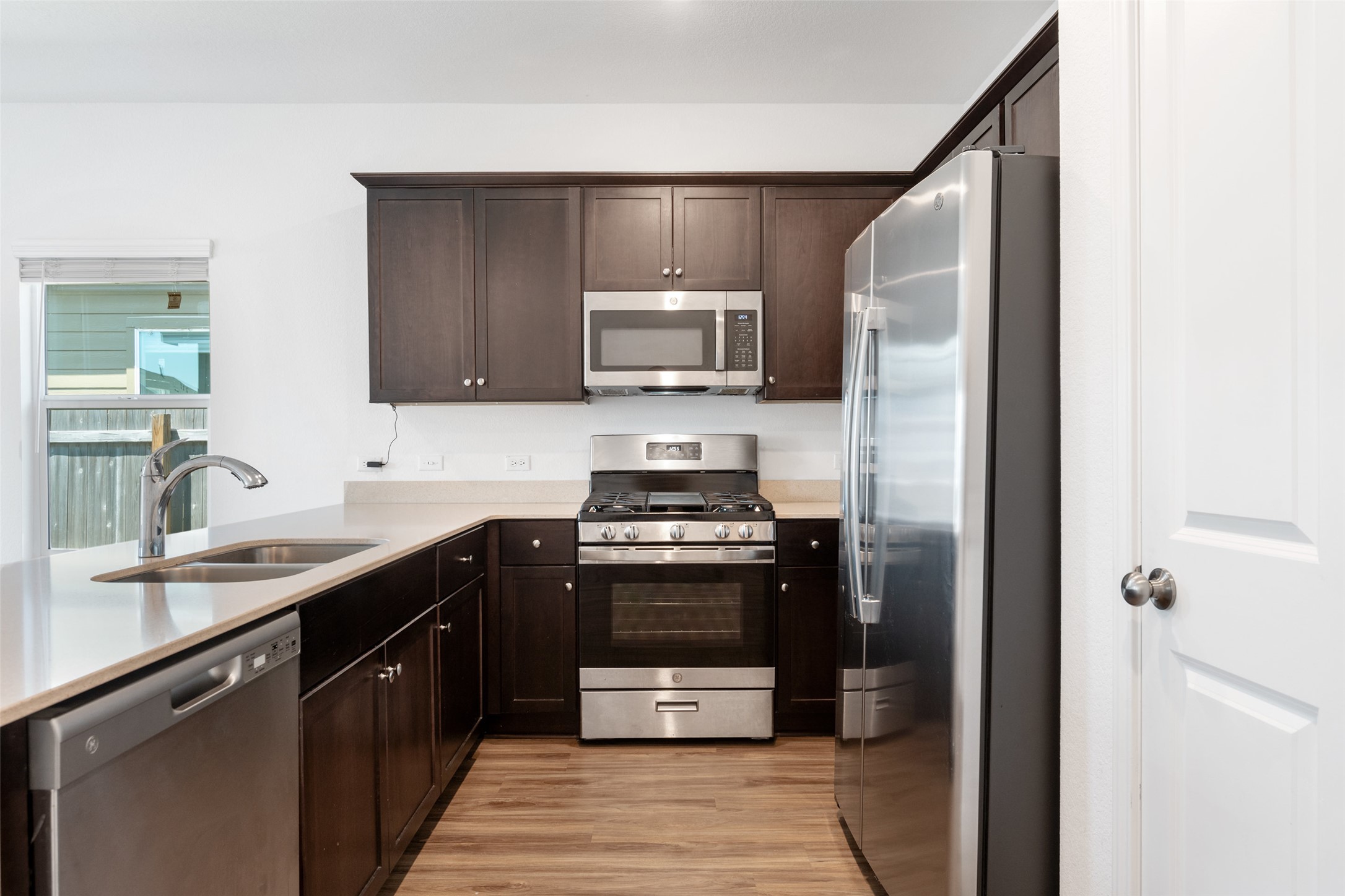 13803 Tordillo Drive Elgin, TX 78621 - Photo 5 of 39 Kitchen featuring stainless steel appliances, dark brown cabinetry, light wood-type flooring, and light stone countertops