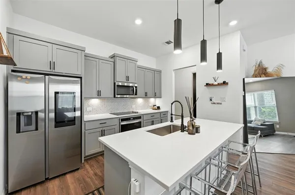 a kitchen with stainless steel appliances a refrigerator a stove a sink a dining table and chairs with wooden floor