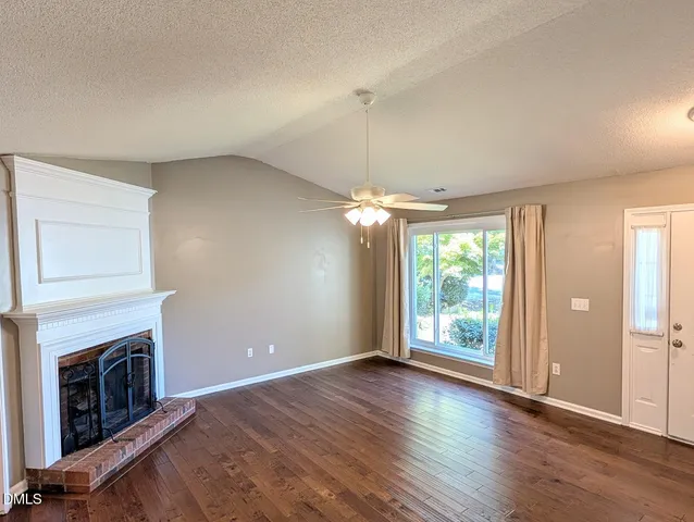 an empty room with wooden floor fireplace and windows