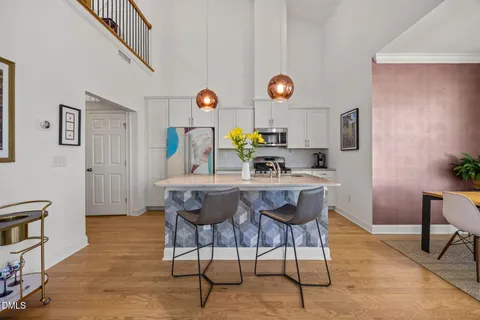 a kitchen with stainless steel appliances granite countertop a stove a refrigerator a kitchen island a dining table and chairs with wooden floor